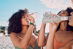 Beach, friends and African women drink bottle of liquid cold drink to relax on Summer vacation in Nigeria. Nature travel, black woman or thirsty bikini girl drinking lemonade on holiday adventure