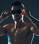 Fitness, sports and face of swimmer with goggles isolated in studio for wellness, exercise and training. Workout, swimming athlete and man focus on dark background with muscle, strong body and tattoo