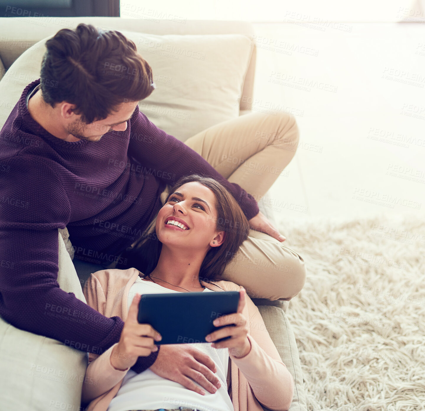 Buy stock photo Shot of a smiling young couple using a digital tablet while relaxing together on the sofa at home