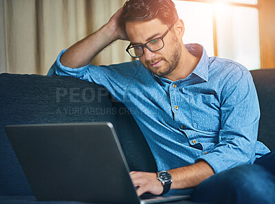 Buy stock photo Shot of a young man using a laptop on the sofa at home