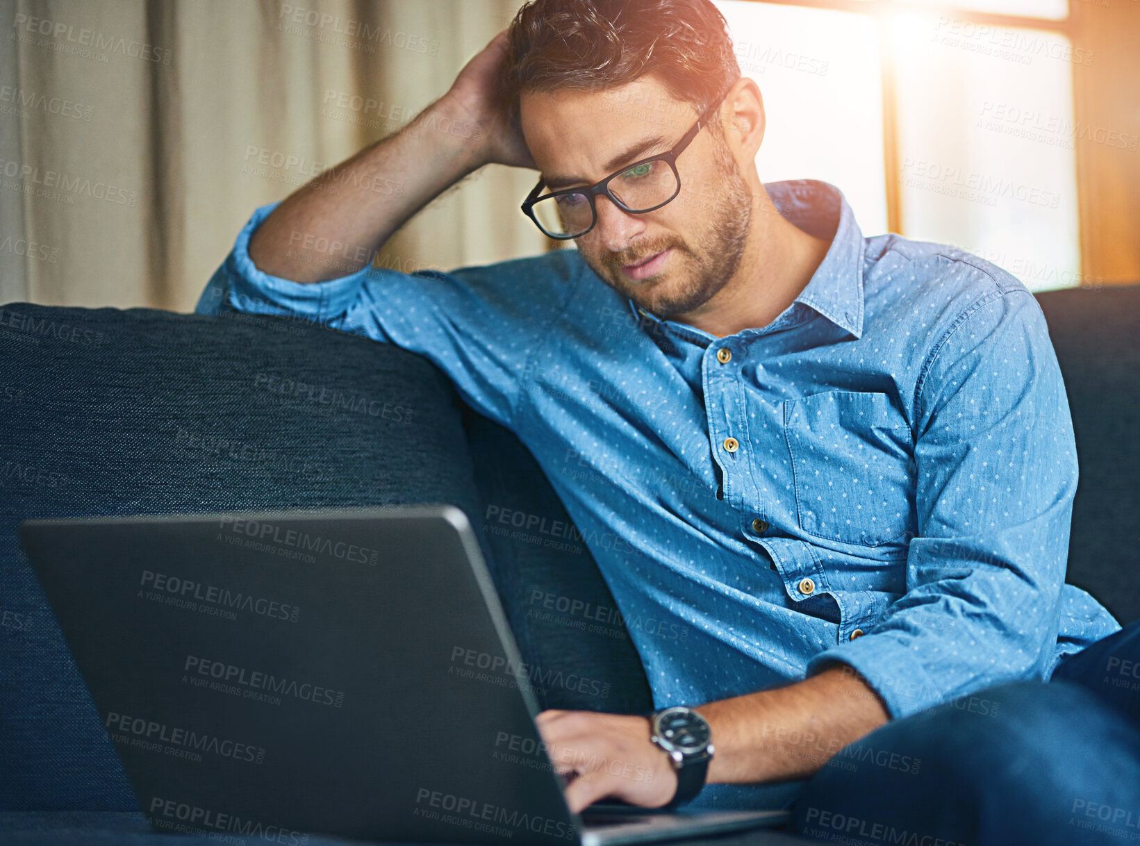 Buy stock photo Shot of a young man using a laptop on the sofa at home