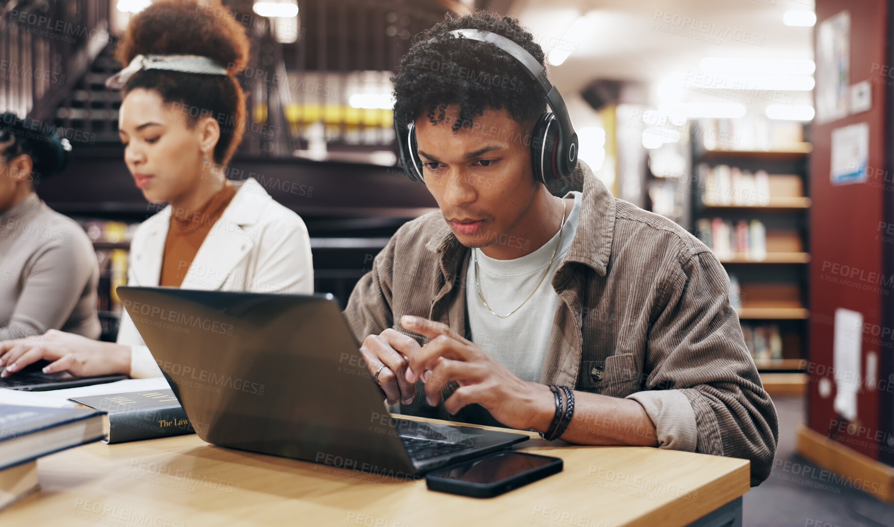 Buy stock photo Man, studying or laptop in library with headphones, problem solving or working on research assignment. Student group, concentration music or tech at college for education, online course or learning