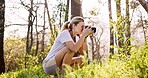 Woman, photographer and nature with camera for sightseeing, bird watching or observation in forest. Young, female person or hiker with photography in woods for picture, memory or outdoor photoshoot