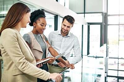 Buy stock photo Shot of a group of colleagues talking together over a digital tablet while standing in a large modern office