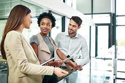 Buy stock photo Shot of a group of colleagues talking together over a digital tablet while standing in a large modern office