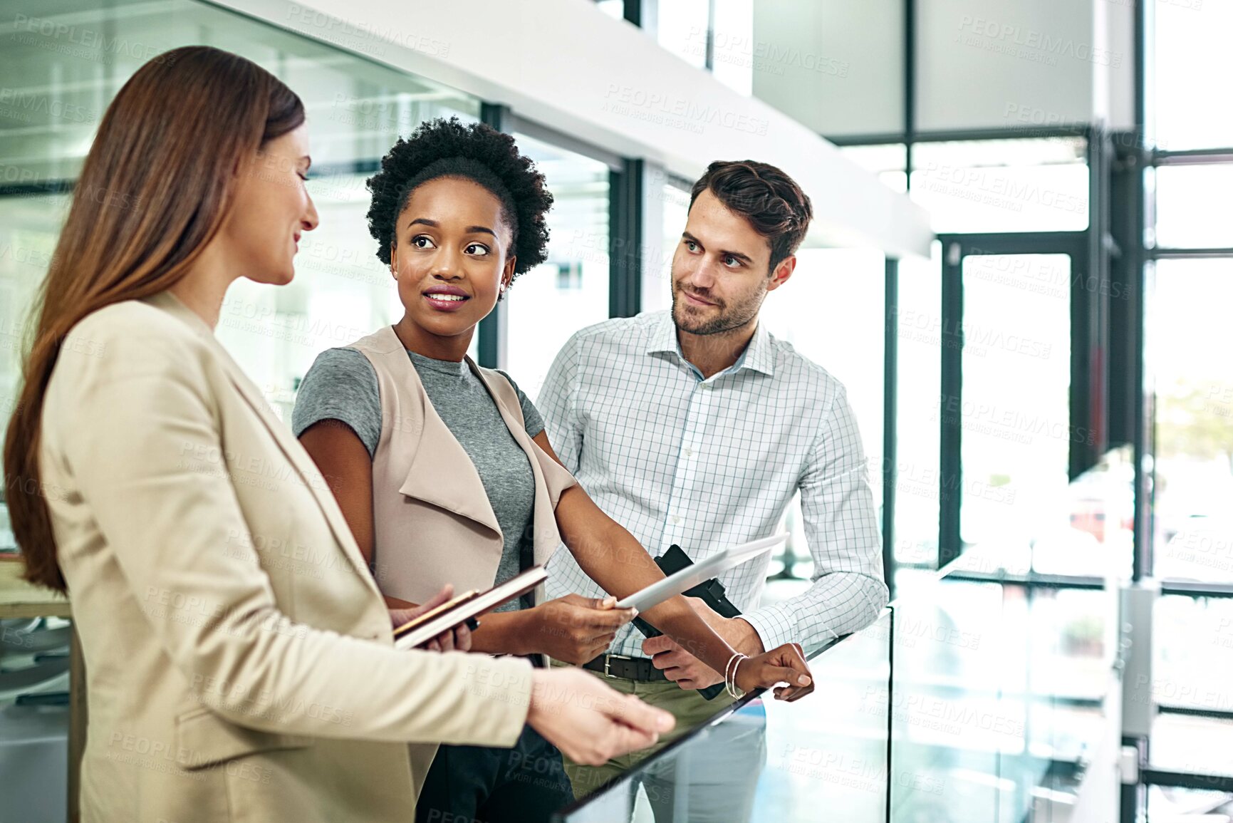 Buy stock photo Shot of a group of colleagues talking together over a digital tablet while standing in a large modern office