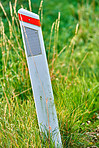 Grass, mile marker and road side with reflector on wooden pole closeup in ground to measure distance. Background, earth and travel with checkpoint in summer countryside for adventure or journey