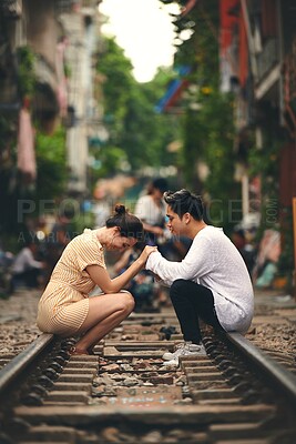 Buy stock photo Interracial couple, travel and holding hands on railway line in city for journey or vacation. Woman, man and bonding at train track in town as holiday, adventure or outdoor fun on platform in Vietnam