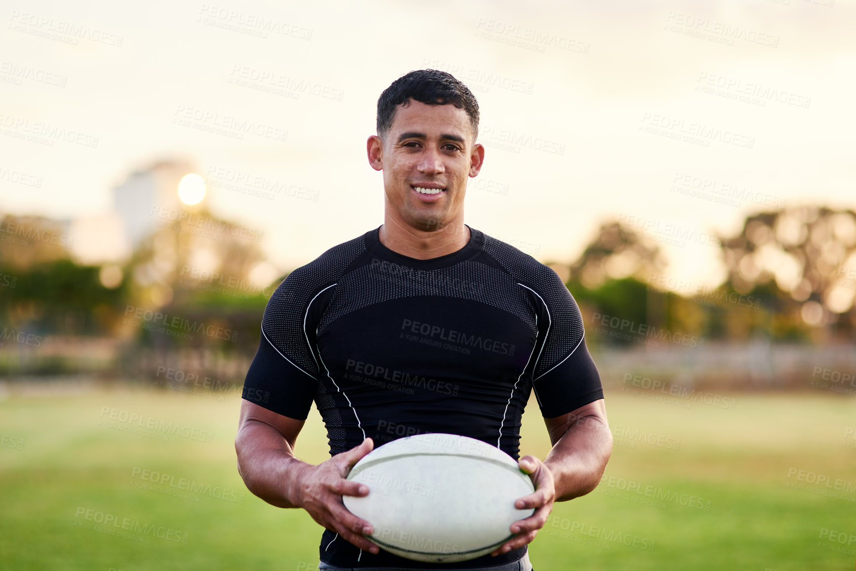 Buy stock photo Rugby, portrait and happy man with ball for game, sports and competition at pitch at sunset. Player, smile and confident athlete at field for body health, exercise and fitness outdoor in Argentina