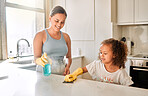 Little girl helping her mother with household chores at home. Happy mom and daughter wearing gloves while spraying and scrubbing the kitchen counter together. Kid learning to be responsible by doing tasks