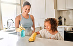 Little girl helping her mother with household chores at home. Happy mom and daughter wearing gloves while spraying and scrubbing the kitchen counter together. Kid learning to be responsible by doing tasks