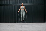 One young african american female athlete skipping using jump rope while exercising outside in the city. Beautiful and dedicated mixed race sportswoman working out alone against an urban background