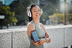 Young mixed race female athlete wearing headphones armband while listening to music  and standing with her arms crossed exercising outside in the city. Positive, happy, workout