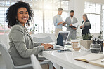 Portrait of a cheerful mixed race businesswoman working on a laptop at work. Happy hispanic female businessperson with a curly afro typing en email on a laptop in an office