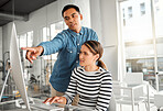 Two businesspeople working on a desktop computer together at work. Young asian male manager training a new employee in an office. Female businesswoman getting help from her boss at work