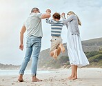 Happy caucasian parents from the back holding hands with their cute little playful son and swinging him up at the beach. Cheerful kid jumping and having fun while bonding with mom and dad on family summer vacation together