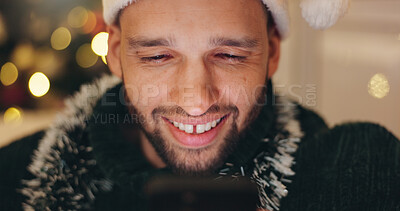 Buy stock photo Man, smile and relax with phone on Christmas for social media, update and online post at home. Santa hat, happy and male person with technology in living room for celebration, chat or festive message