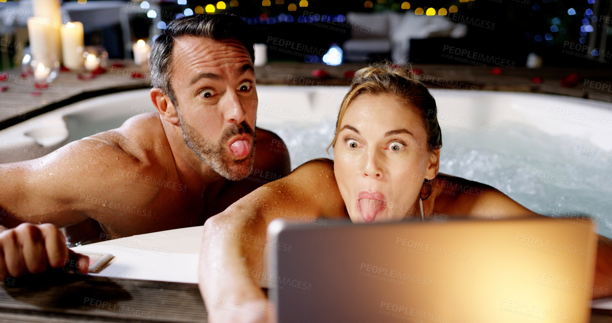 Buy stock photo Couple, hot tub and selfie with tablet, funny face and night on holiday, love or post on web at luxury resort. Woman, man and tongue out for memory, app and comic profile picture for social network