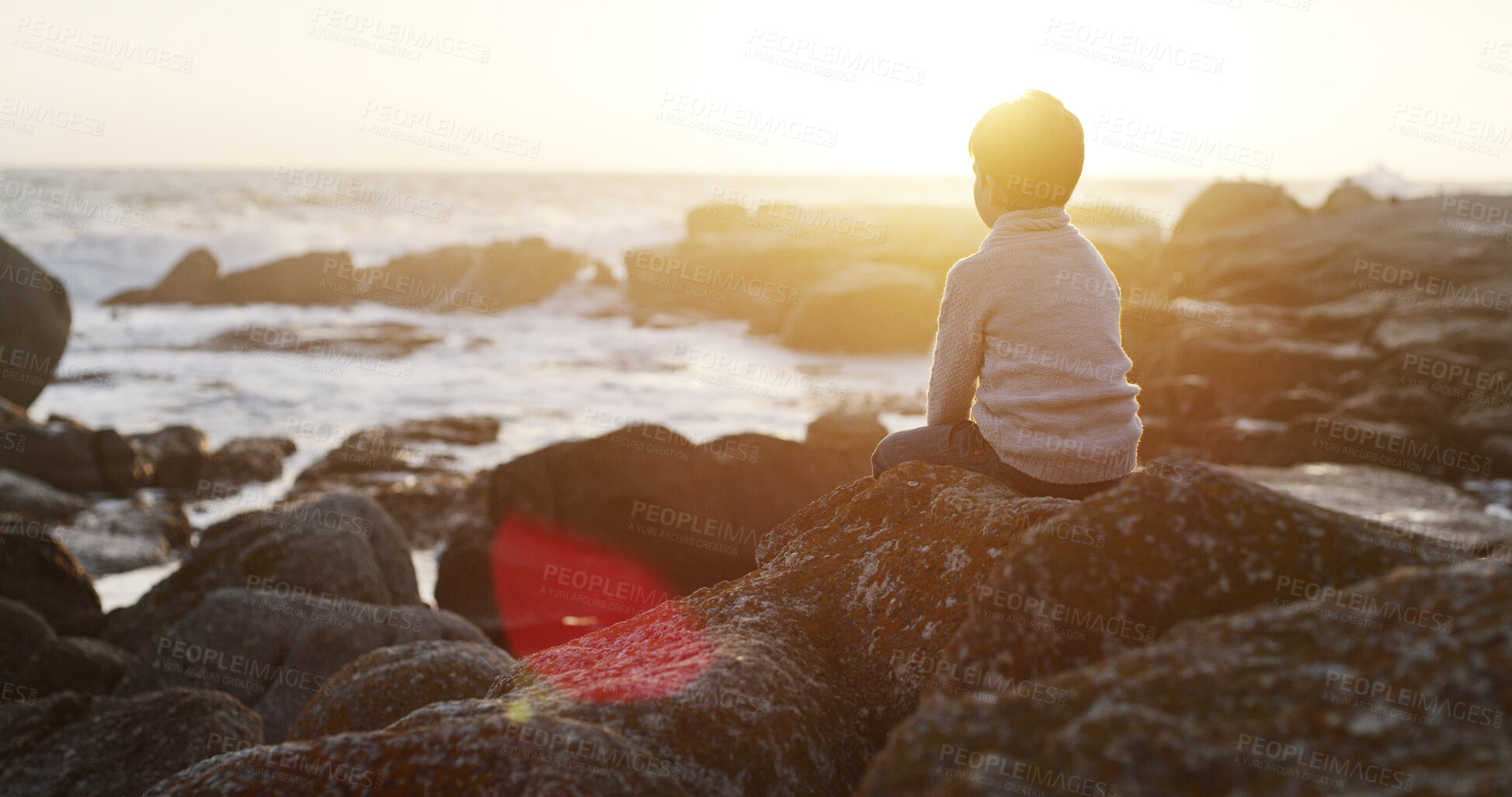 Buy stock photo Child, outdoor and rock by sea with thinking, sunrise and relax at morning in nature on holiday. Vacation, back and beach with idea, lonely and loss of young kid on stone by waves with abandonment