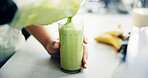 Hands, person and pour liquid in glass in kitchen with organic ingredients, vegan smoothie and nutrition drink. Green juice, blender and healthy beverage, diet breakfast and protein shake at house
