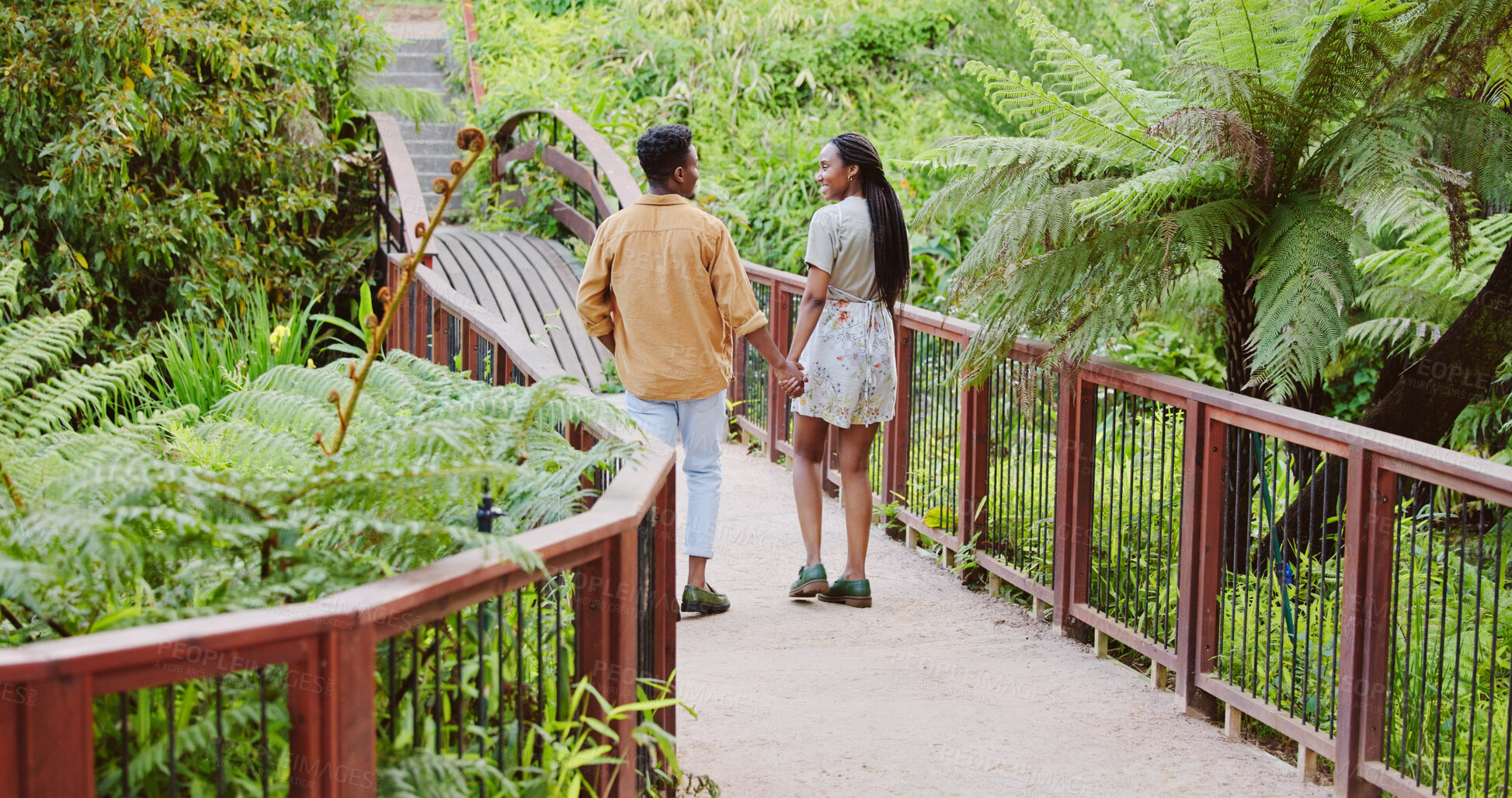 Buy stock photo Walk, nature and black couple holding hands on bridge in park for bonding, connection and outdoor adventure. Love, man and woman on wooden path for romantic date, weekend and green garden from back
