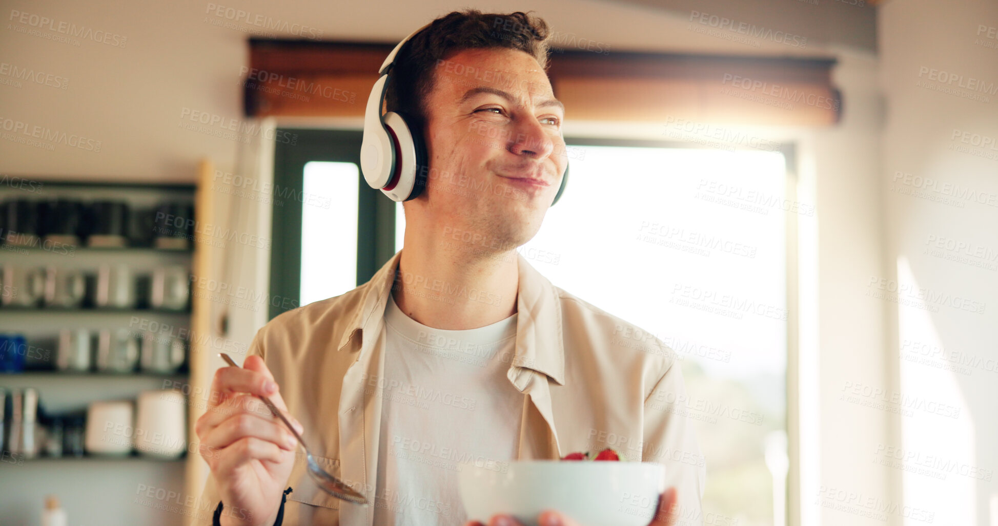 Buy stock photo Headphones, eating and man with healthy breakfast in kitchen listening to podcast in morning for self care. Audio tech, happy and person enjoying fruit salad for diet, nutrition or wellness in home.