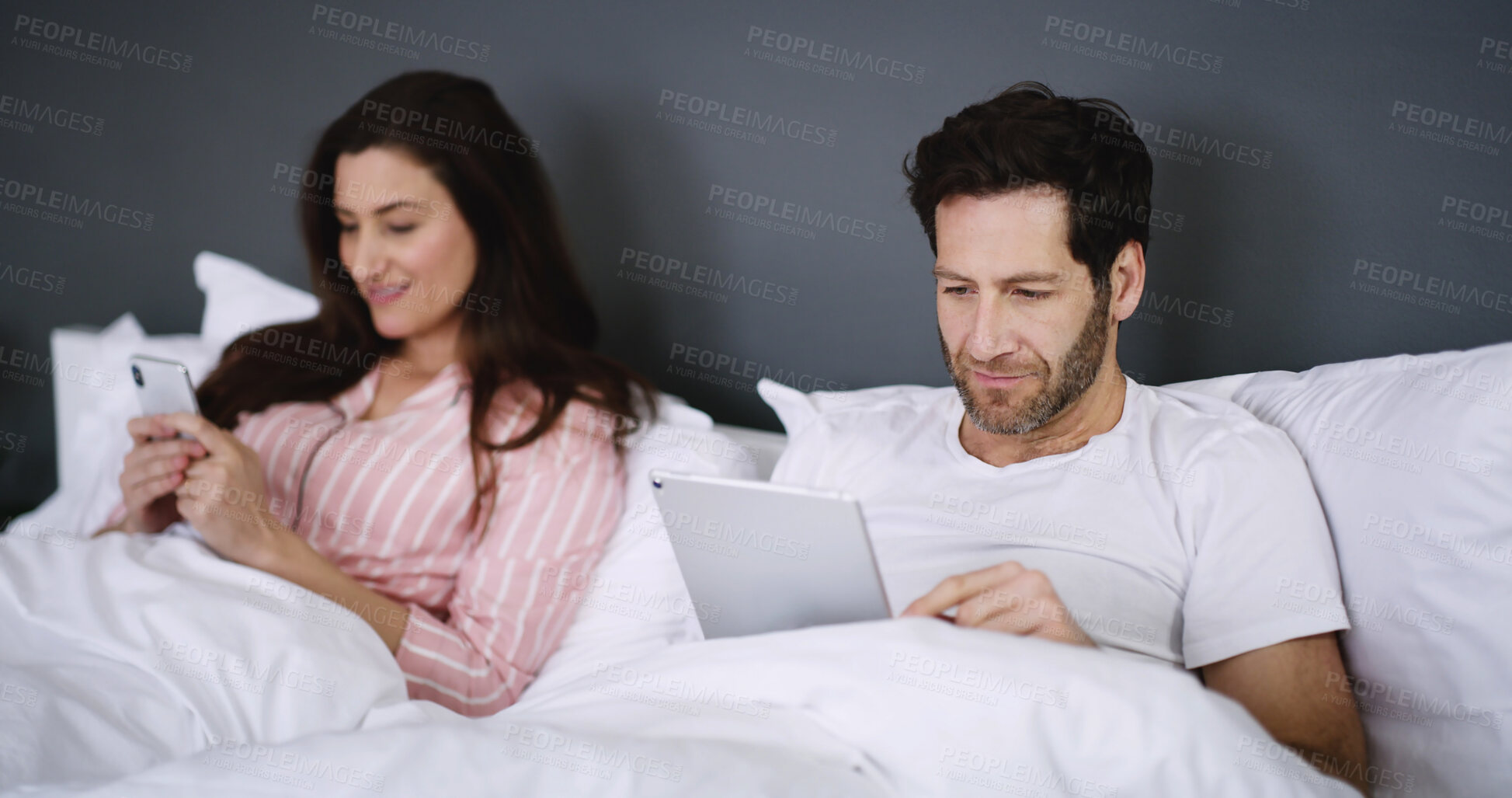 Buy stock photo Phone, tablet and couple relaxing in bed in home for networking, connectivity or browsing online. Happy, rest and young people with cellphone and digital technology in bedroom for contact in house.