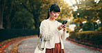 Japanese woman, walking and phone in park for online networking, dating app or travel with mobile chat. Person, smartphone and smile for social media post, notification or browsing internet in street