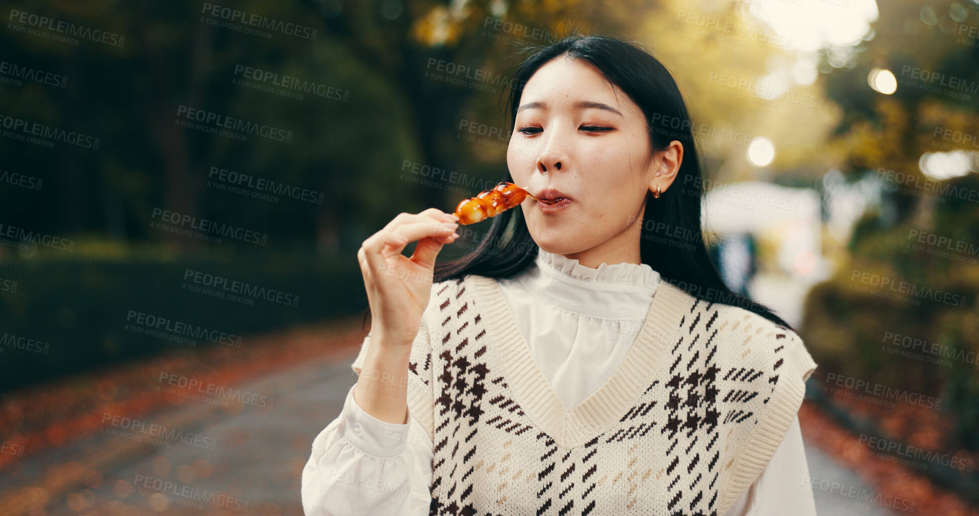 Buy stock photo City, japanese woman and eating street food in park for traditional dessert, lunch and cultural cuisine. Tourist, hungry person and enjoyment with dango dumpling, skewer snack and sweets taste test