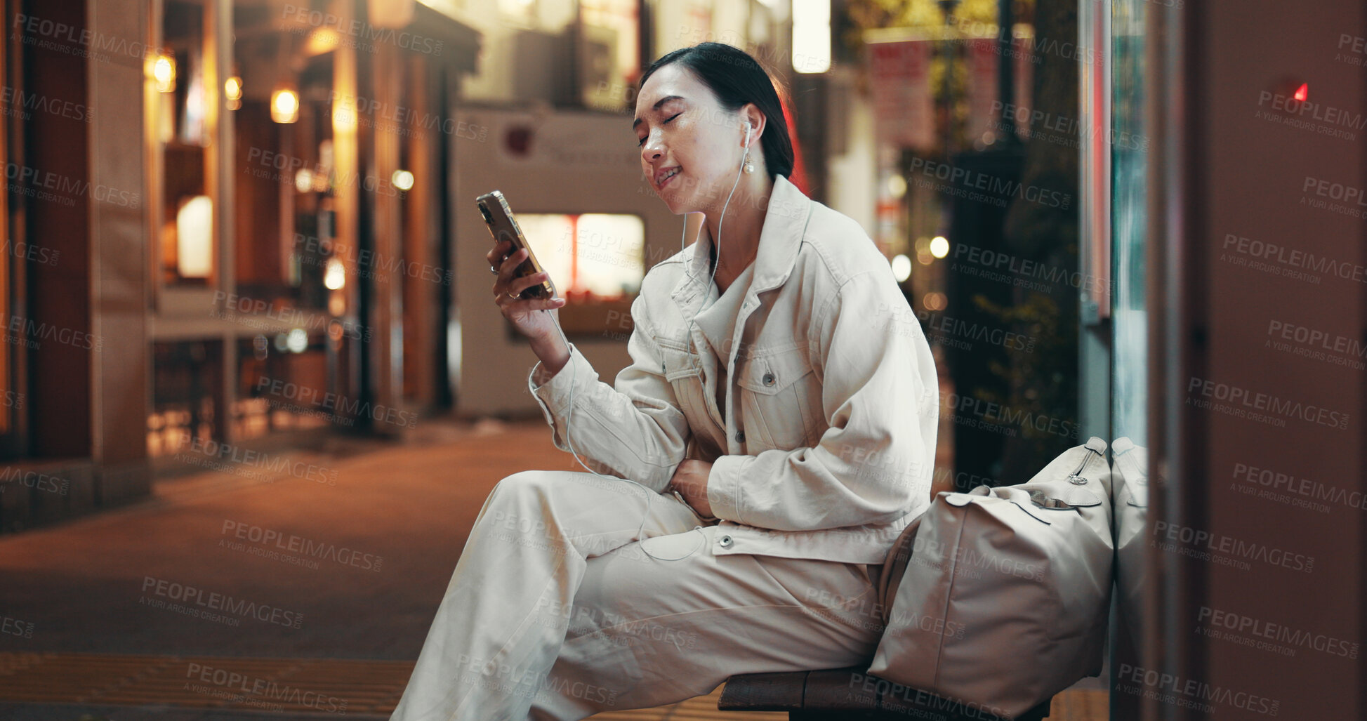 Buy stock photo Night, earphones and woman at bus stop with phone, travel and checking online public transport schedule in city. Smartphone, search and Japanese girl with mobile app, music and late urban commute