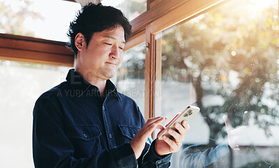 Buy stock photo Japanese, man and typing with phone at house for communication, social media and reading online blog. Male person, window and scroll on mobile with contact, website research and morning news in Japan