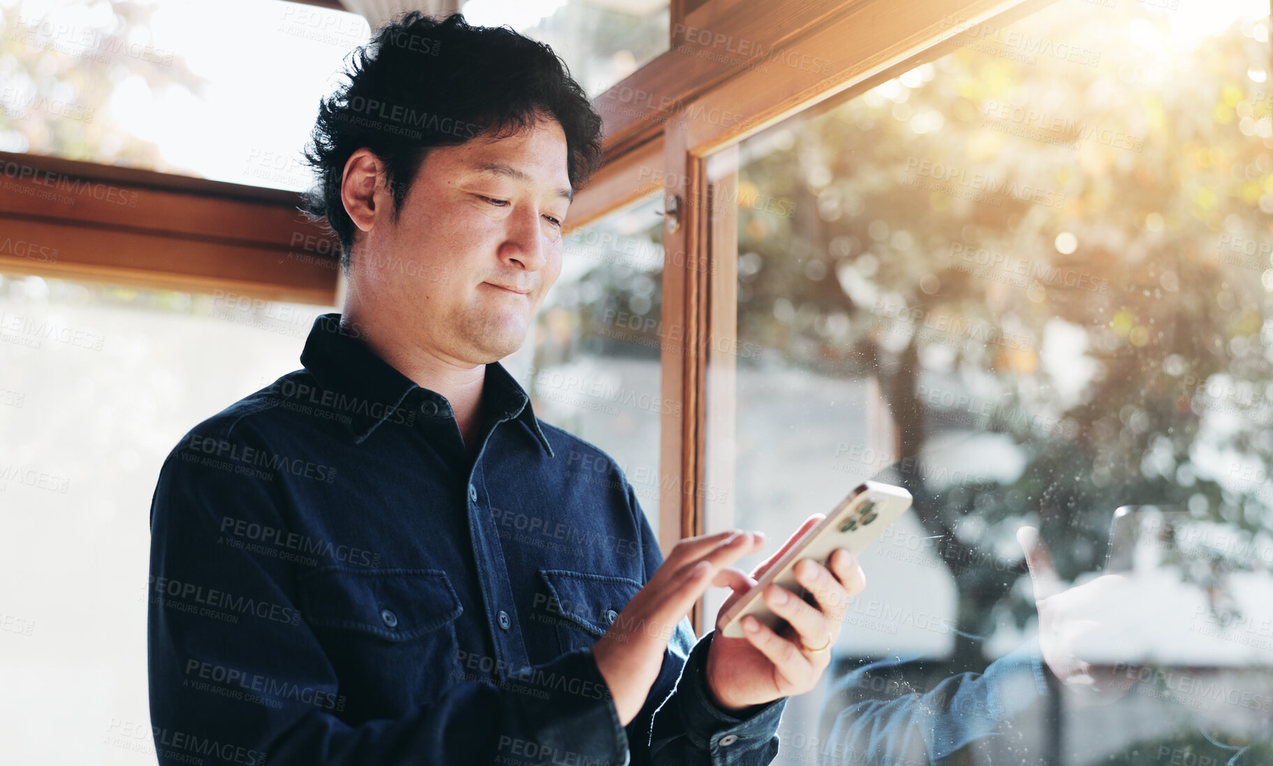 Buy stock photo Japanese, man and typing with phone at house for communication, social media and reading online blog. Male person, window and scroll on mobile with contact, website research and morning news in Japan