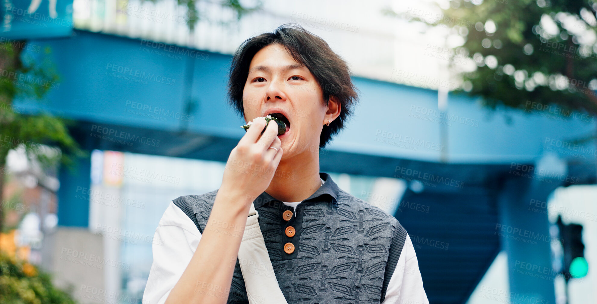 Buy stock photo Asian man, eating and street food in city for travel, hungry and traditional snack on afternoon commute in Japan. Student, walk and onigiri in Tokyo for lunch, wellness and local meal with culture