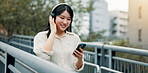 City, happy woman and headphones for music on mobile, streaming podcast or travel. Phone, outdoor and Japanese girl listening to audio on internet, sound and jazz song on radio app online on bridge