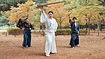 Martial arts, people and instructor with wood sword for fight, battle and samurai training class. Park, ninja and mentor with bamboo weapon, kendo and warrior in autumn in Japan with fighter group