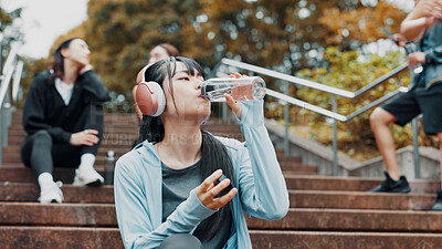 Buy stock photo Woman, headphones and drinking water for training in park, mineral liquid and fitness recovery. Female person, athlete and nutrition for hydration on stairs, workout break and streaming song in Japan