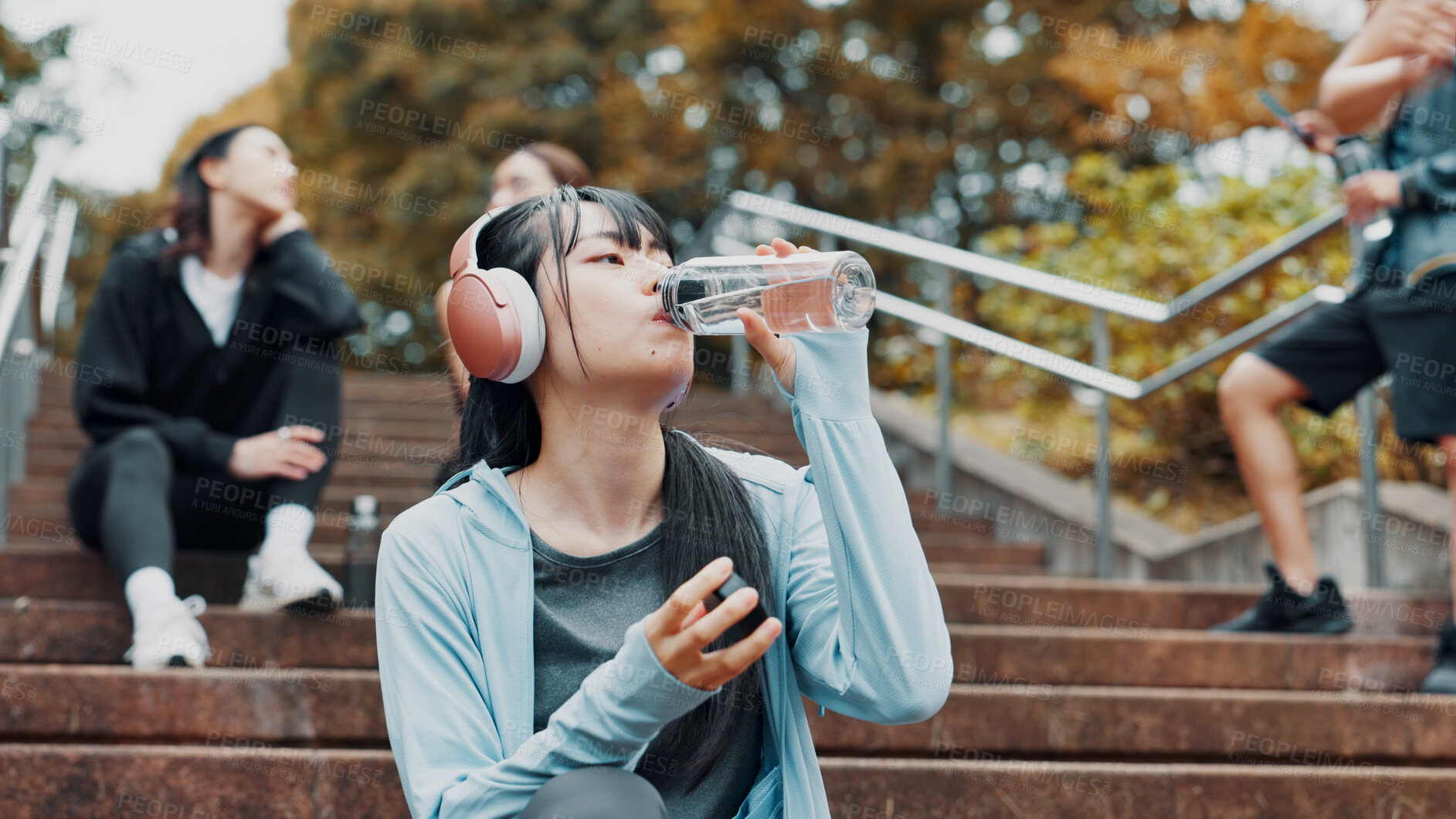 Buy stock photo Woman, headphones and drinking water for training in park, mineral liquid and fitness recovery. Female person, athlete and nutrition for hydration on stairs, workout break and streaming song in Japan