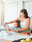 Cheerful mother and little daughter having fun cooking together in the kitchen. Mom and child cutting vegetables preparing a vegetarian meal