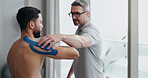 Physiotherapist, patient and tape at clinic for shoulder pain, recovery or support for healthcare service. People, help and advice with application for injury, muscle and rehabilitation at hospital