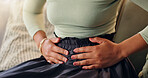 Hands, menstruation and stomach pain with woman on sofa in living room of home for menstrual cramps. Fertility, ovulation cycle or phase and person closeup in apartment with symptoms of monthlies