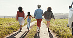 Family, friends and child holding hands for walking in park together on summer holiday or vacation. Back, bonding or love and group of people outdoor in field of flowers for getaway or road trip