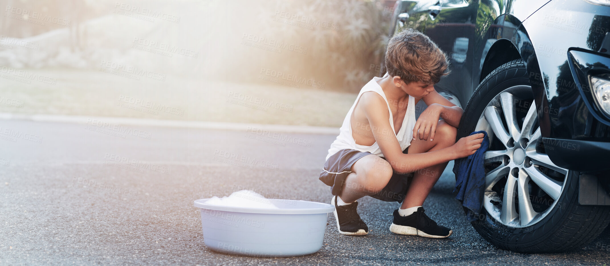 Buy stock photo Washing car, driveway and kid with cloth for cleaning vehicle for summer job, learning and responsibility. Housework, chores and boy with supplies for polish, wipe and dust wheels for maintenance