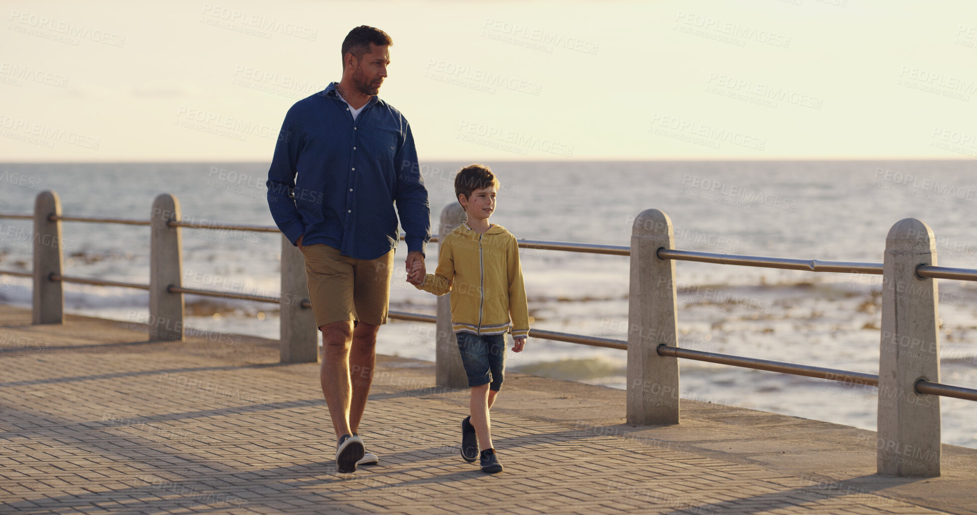 Buy stock photo Father, son and holding hands at sea on holiday, walking and outdoor for bonding with daddy. Boy, child and papa for vacation security on promenade, together and ocean for love or connect on trip
