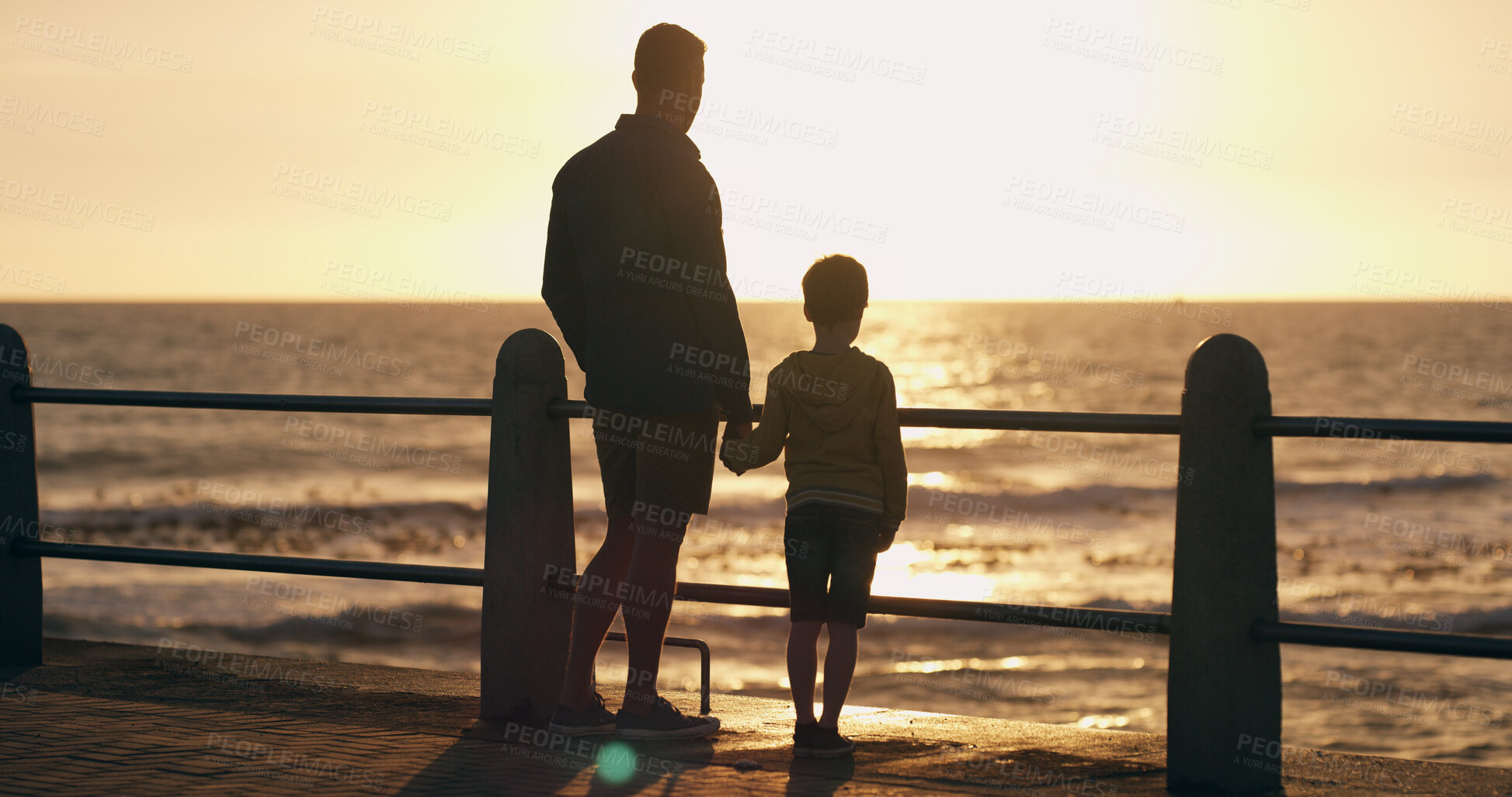 Buy stock photo Father, son and holding hands at sunset on beach, walking and outdoor for bonding with daddy. Back, child and papa for sightseeing on promenade, together and ocean view for love or connect on trip