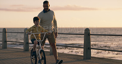 Buy stock photo Dad, boy and bike at sunset, beach and promenade with teaching, support and happy on vacation. Father, child and bicycle with learning, adventure and playful with bonding by ocean in Australia