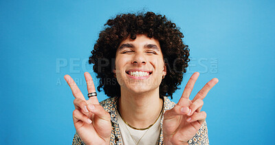 Buy stock photo Happy man, peace sign and eyes closed with positive, expression for funky or hipster attitude on a blue studio background. Male person, young model or smile with emoji or finger gesture for V symbol