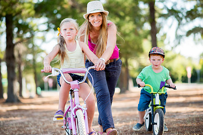 Buy stock photo Mother, children and outdoor for riding bicycle, learning development and practice in neighborhood. Happy, bike and kids for travel adventure on weekend, mom helping and holiday for childhood play