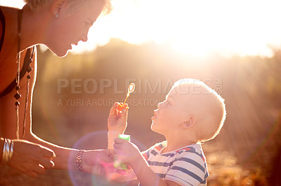 Buy stock photo Happy, blowing bubbles and child in nature with mom for fun, childhood and bonding together outdoors. Family, sunlight and woman with young boy with soap wand, toys and activity for playing in park
