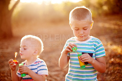 Buy stock photo Happy, blowing bubbles and kids in park for fun, childhood and bonding together outdoors. Family, sunlight and young brothers with soap, toys and activity for playing, adventure or game in nature