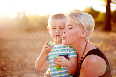 Buy stock photo Family, blowing bubbles and child in nature with mom for fun, childhood and bonding together outdoors. Happy, sunlight and woman with young boy with soap wand, toys and activity for playing in park